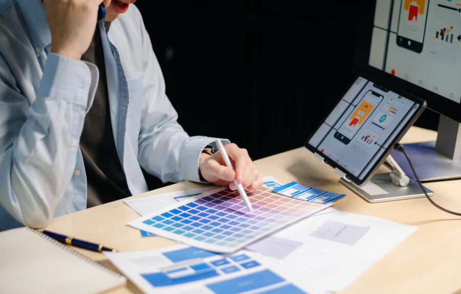 Asian designer’s hands reviewing UX/UI mockups and color palettes at modern desk. App design, user interface, and branding concept with real people.